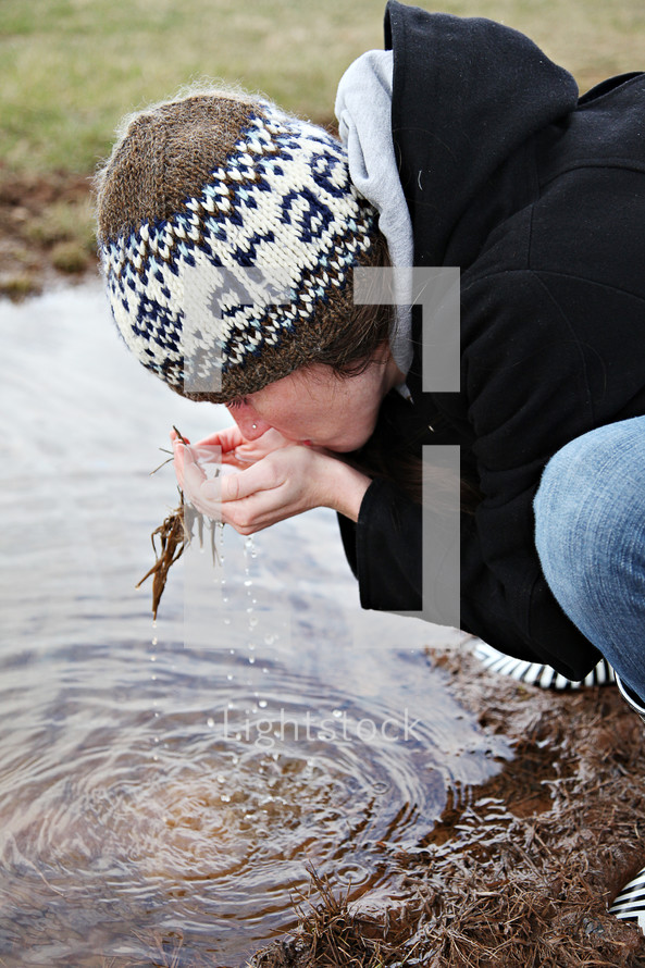 A woman scoops water and drinks from a stream.