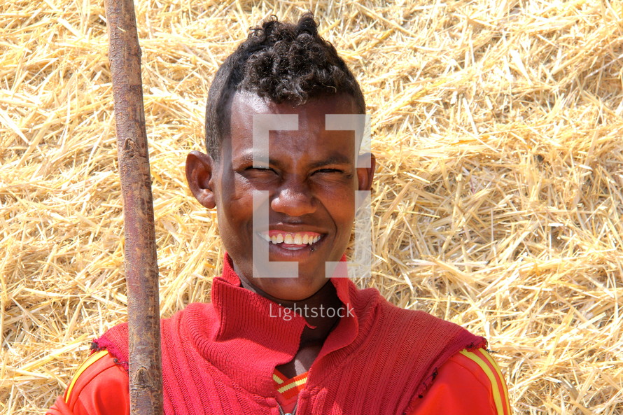 smiling young man holding a pitch fork in front of hay