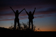 silhouettes of young women on a mountaintop at sunset 