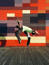 Two people doing back flips in front of a colorful wall.