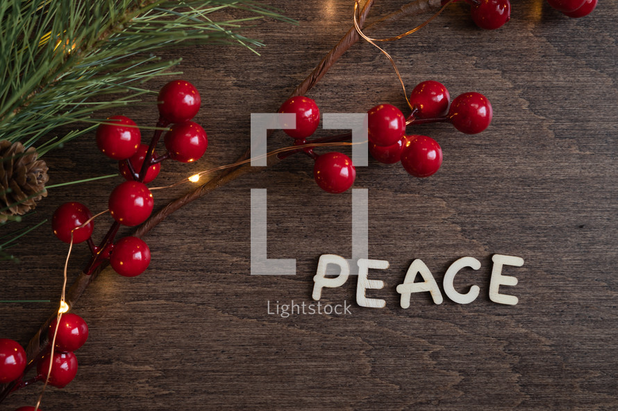 red berries and fairy lights on a wood background and word peace 