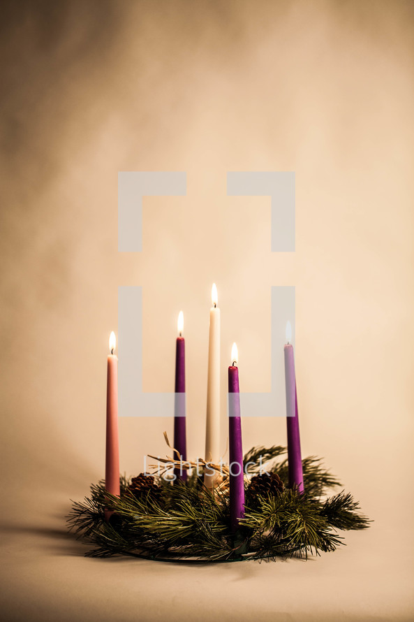 Five lit candles in pine wreath.