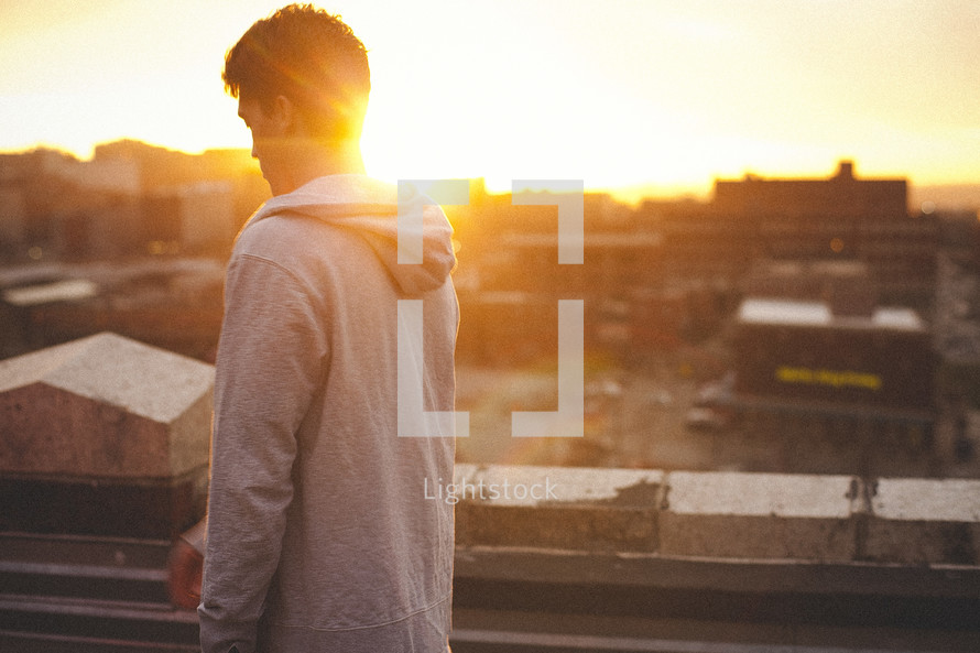young man standing leaning against a ledge on a city rooftop 