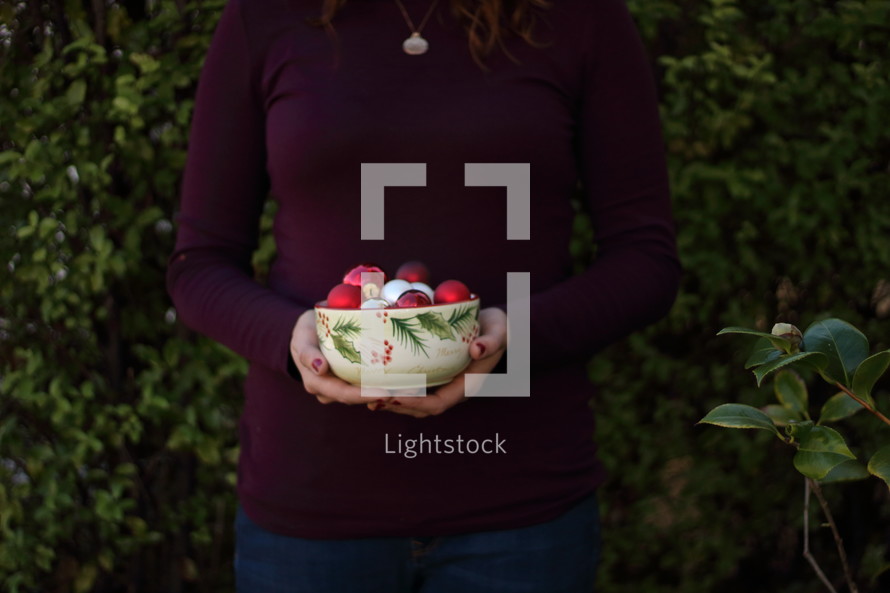 a woman holding a bowl of Christmas ornaments 