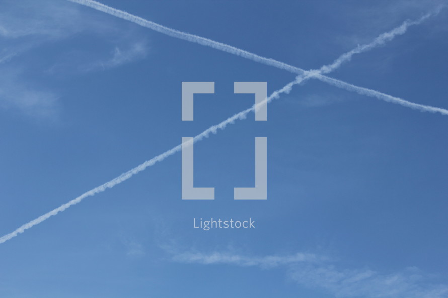 White airplane vapor trails in the blue sky in the shape of a cross
