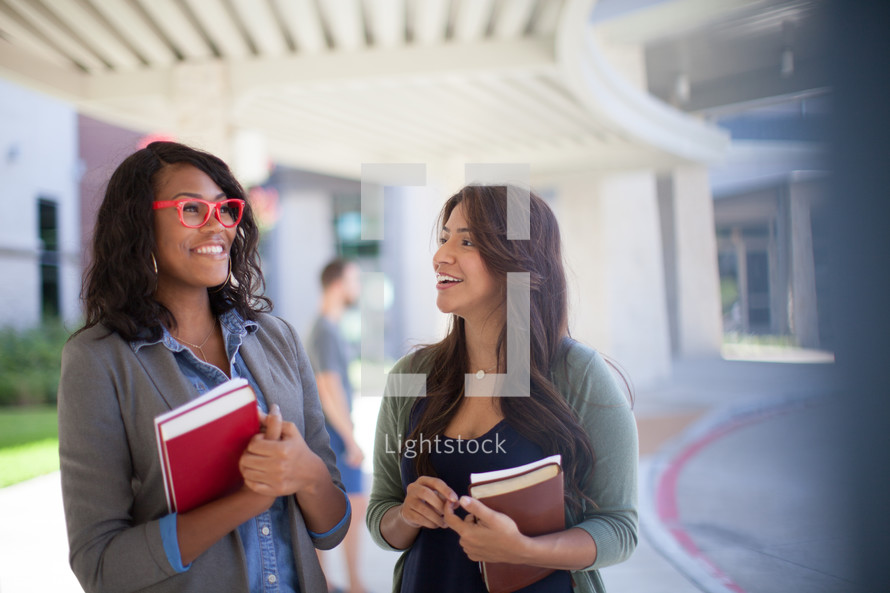 Two young women standing in front of a church with Bibles.