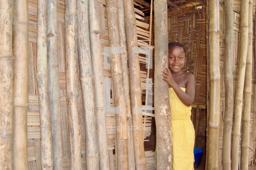 A young African girl peeking out of a bamboo hut 