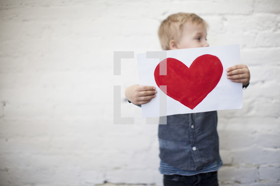 a toddler boy holding a heart painted on paper 