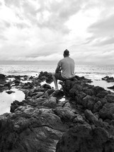 man sitting on rocks along a shore 