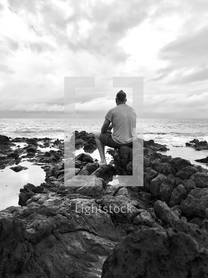 man sitting on rocks along a shore 