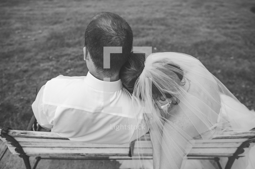 bride and groom sitting on a bench snuggling 
