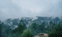 a man standing at the top of a mountain watching fog rise 
