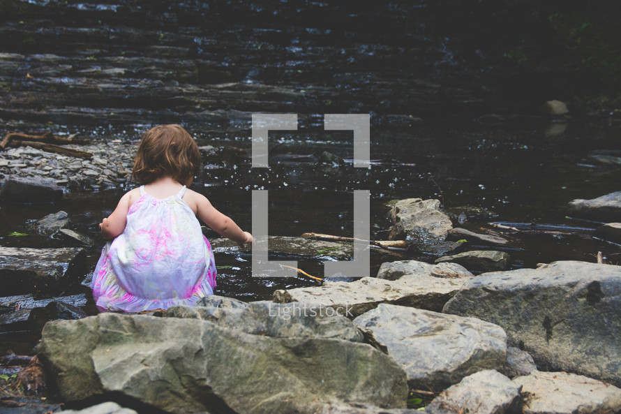 toddler girl playing by the edge of a stream 
