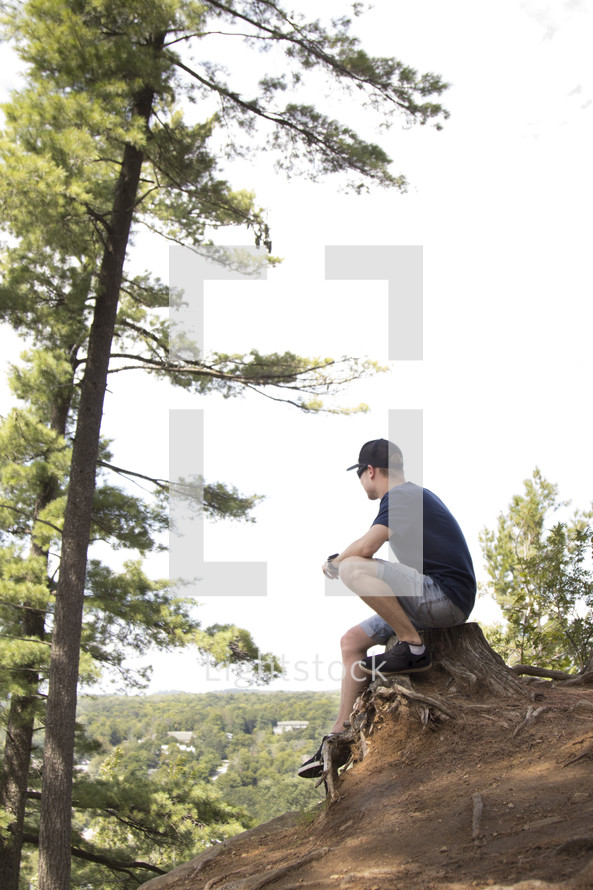 Teenager sitting on stump and praying on high cliff