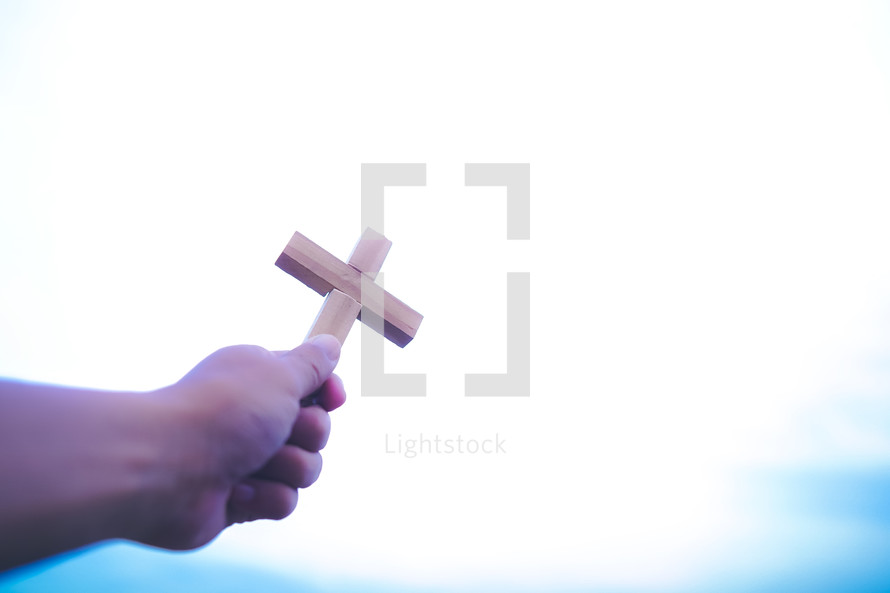 Hand holding a wooden cross up to the sky