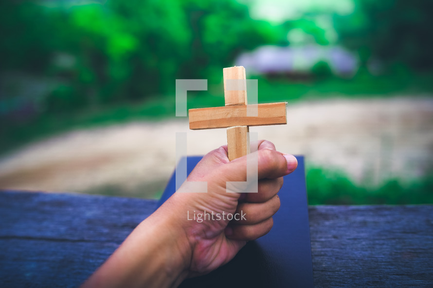 Hand holding a wooden cross on the Bible