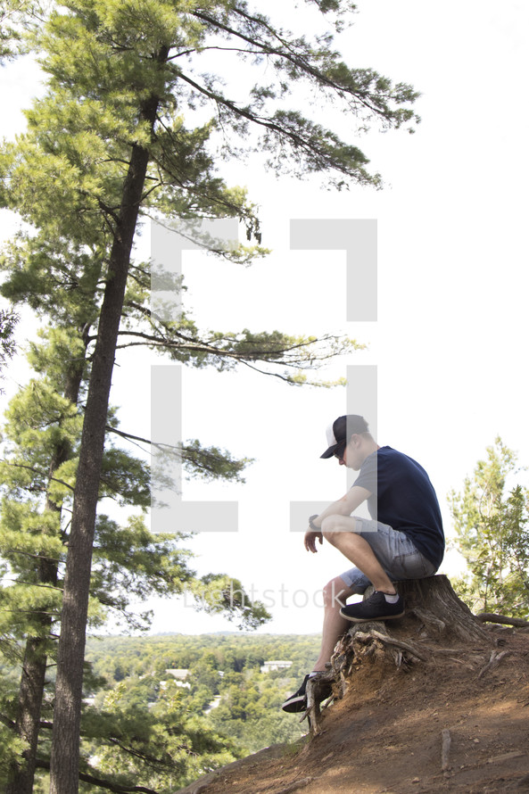 Teenager sitting on stump and praying high up on a cliff area