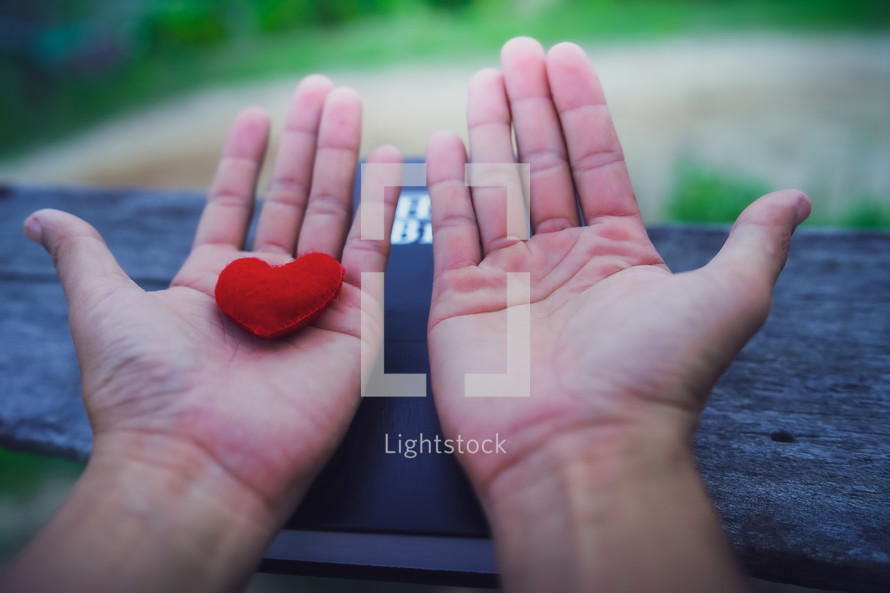 Hands with palms up on a Bible holding a red fabric heart