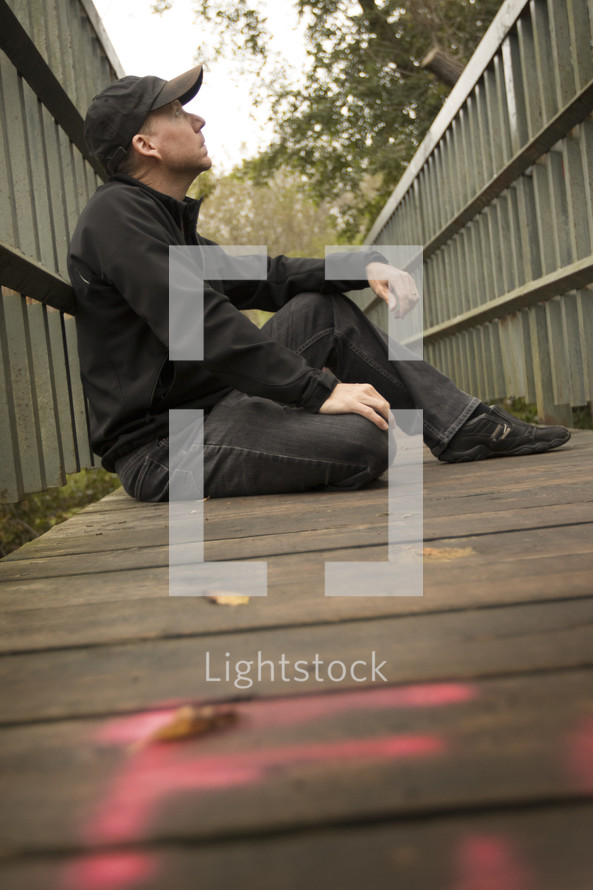 a man sitting on a boardwalk thinking and looking up at the sky 