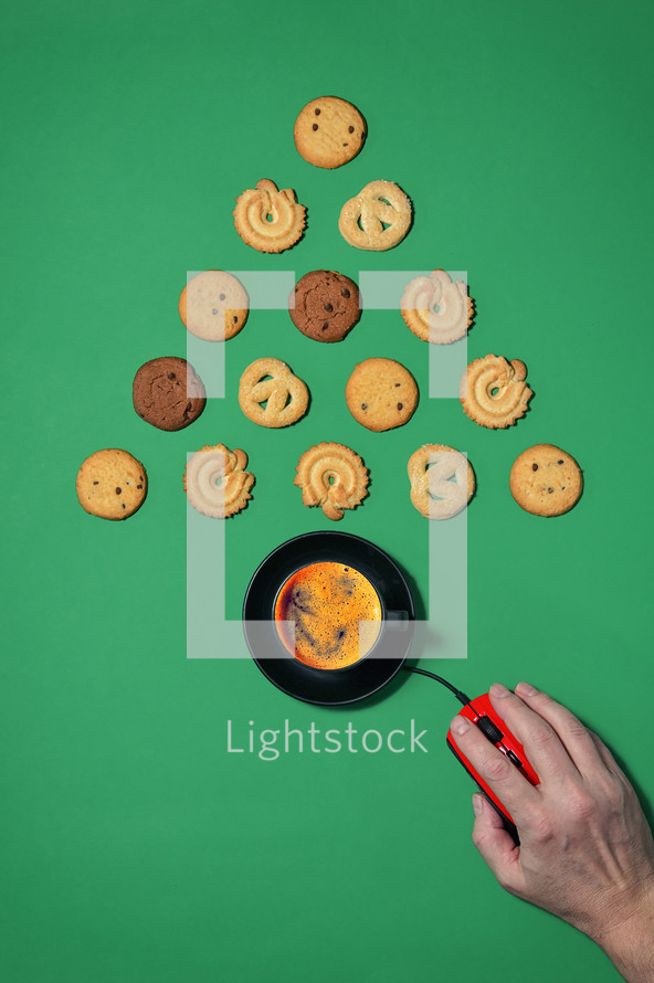 Coffee and cookies in the shape of a Christmas tree with computer mouse and hand on a green background