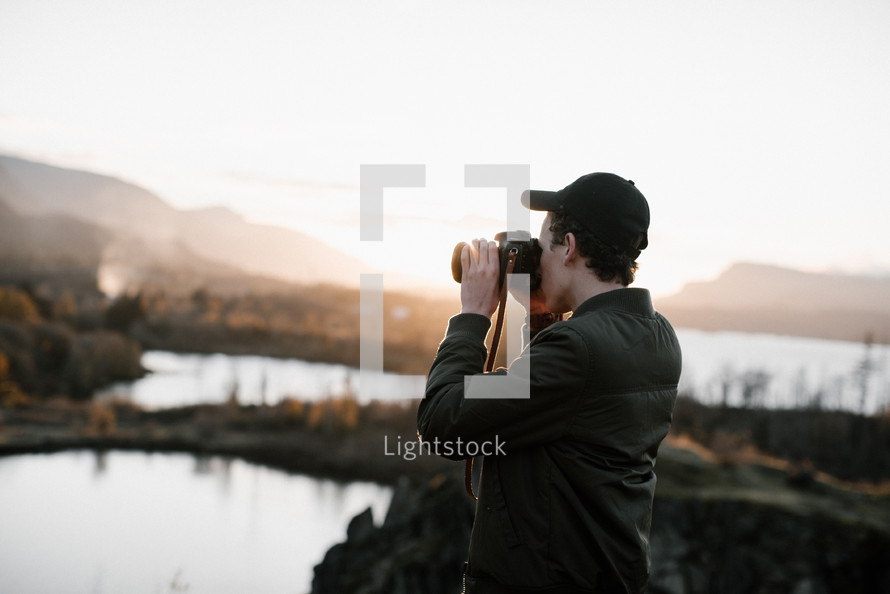 a man with a camera taking a picture of mountains at day break 