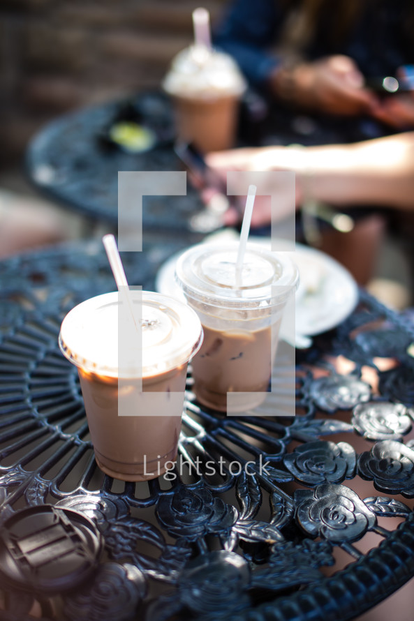 Iced coffee drinks in plastic cups on table at an outdoor bistro cafe.