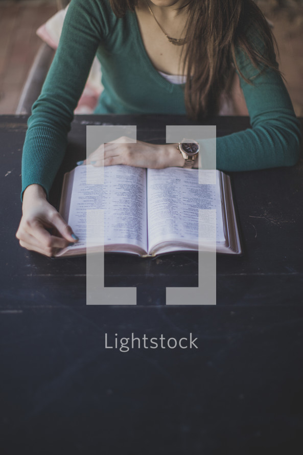A woman sitting at a table reading the Bible