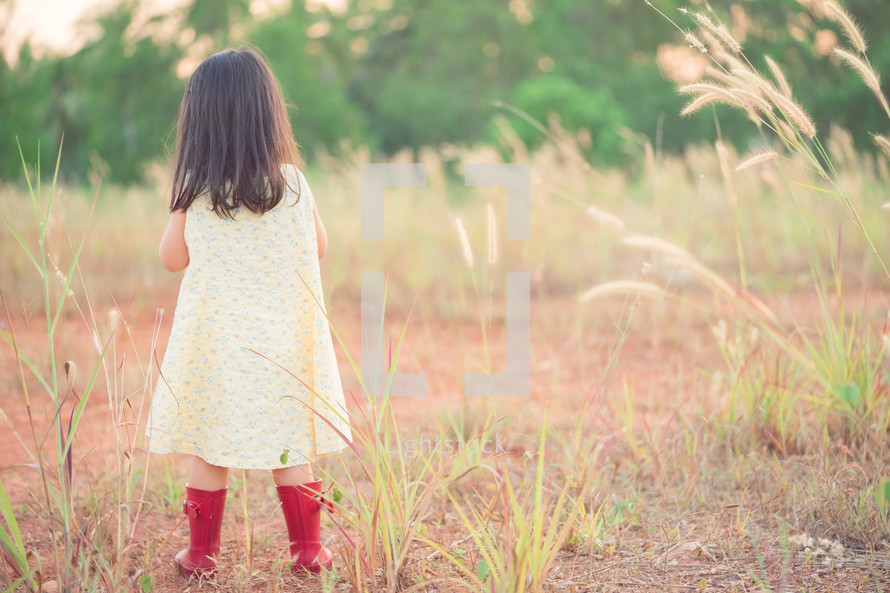 Back view of Little asian girl in a yellow dress and wear red boots waiting 