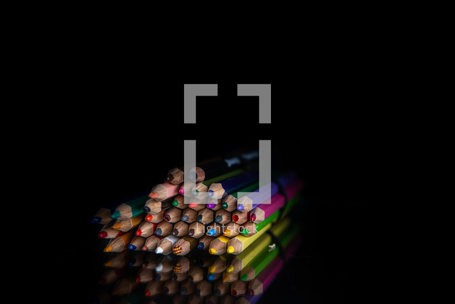 stack of colored pencils on a black background with copy space