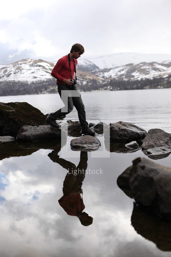 A photographer steps on stones across a body of water.