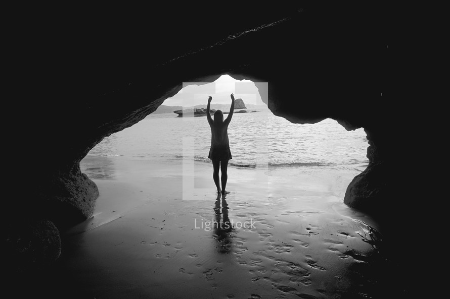 woman with raised hands standing in a cave on a beach 