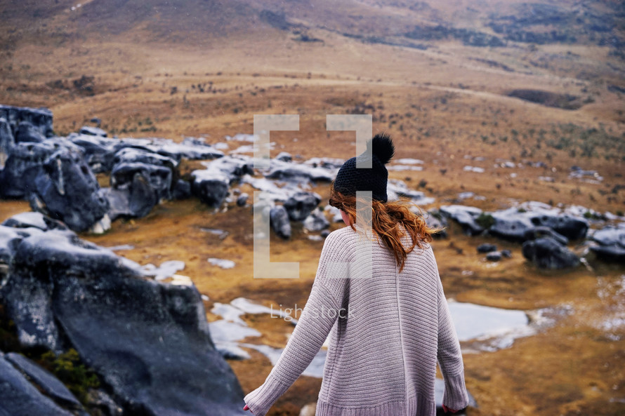 woman in a sweater walking on rocks on a mountain 