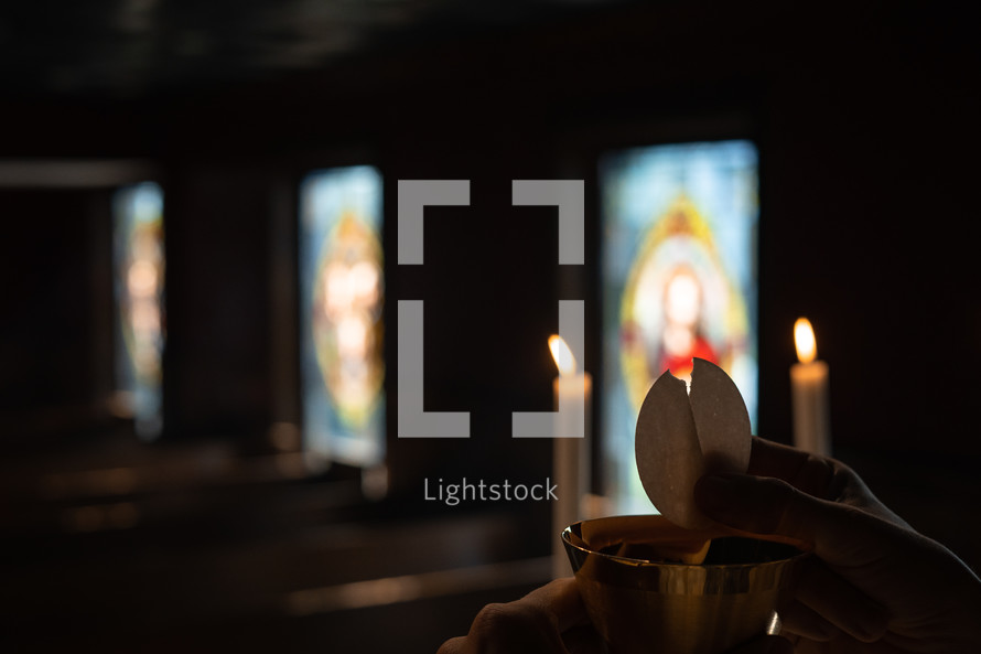 Communion wafer being broken in a candlelit service.  