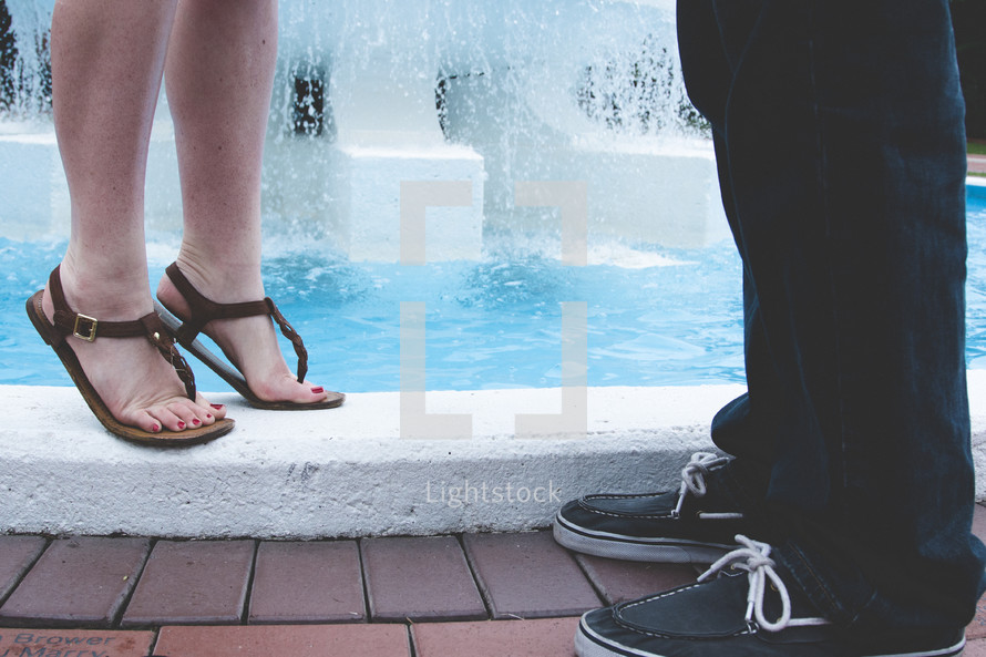 feet of a couple standing near a fountain 