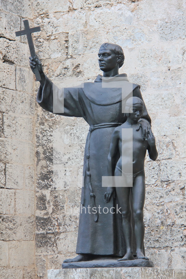 Statue of a priest holding a cross with his arm around a boy.