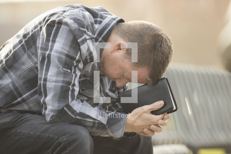 a man with his head down leaning on a Bible 