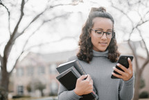 a young woman holding a stack of books and holding a cellphone 