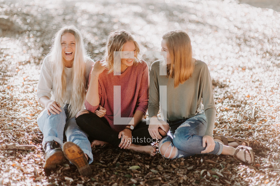 three women sitting on the ground talking 