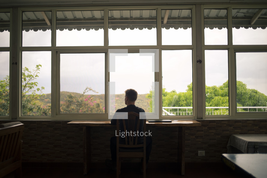a man sitting at a table looking out a window in thought 