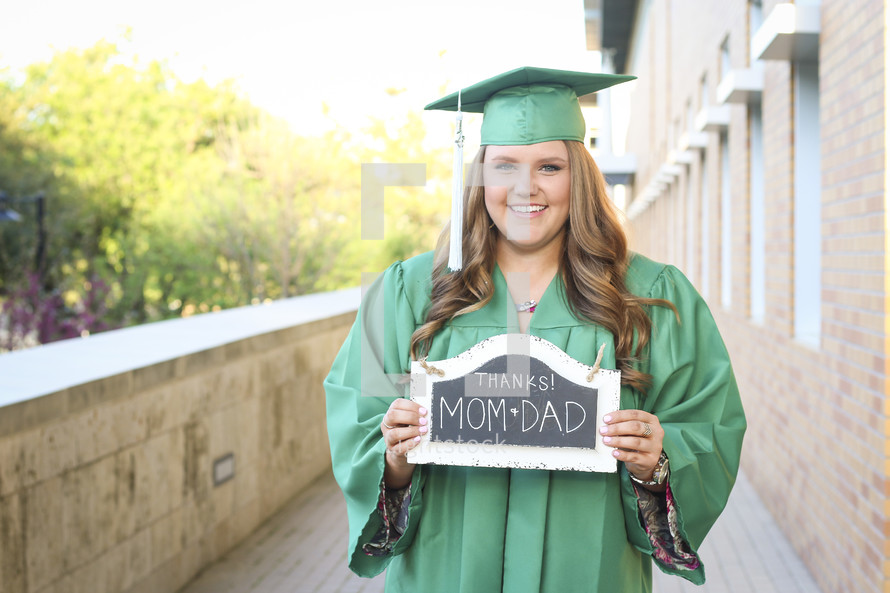 A graduate holding a thanks mom and dad sign 