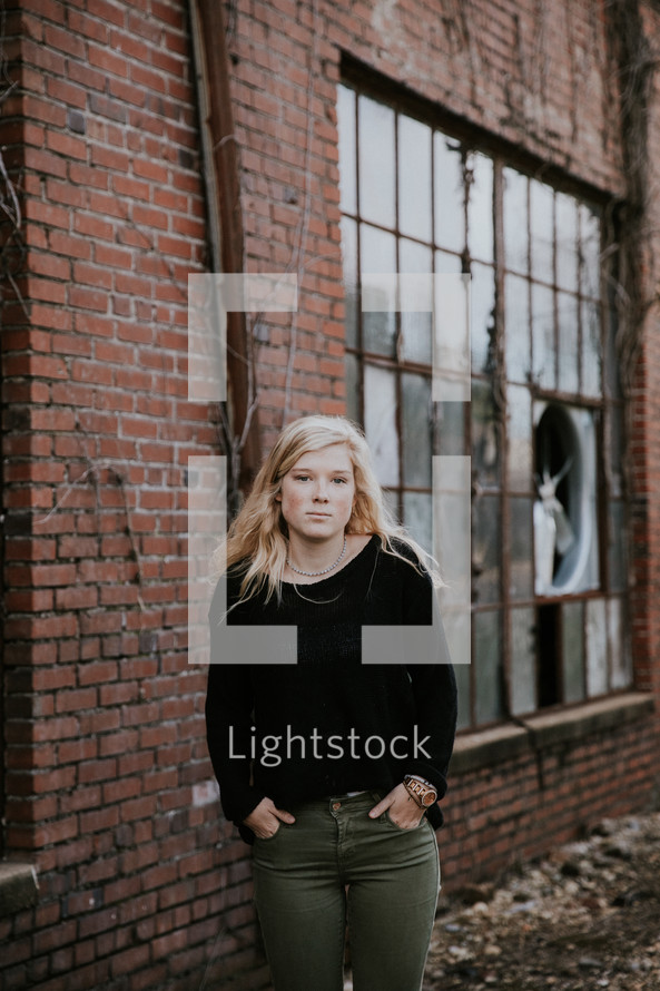 senior portrait of a young woman standing in front of a brick warehouse 