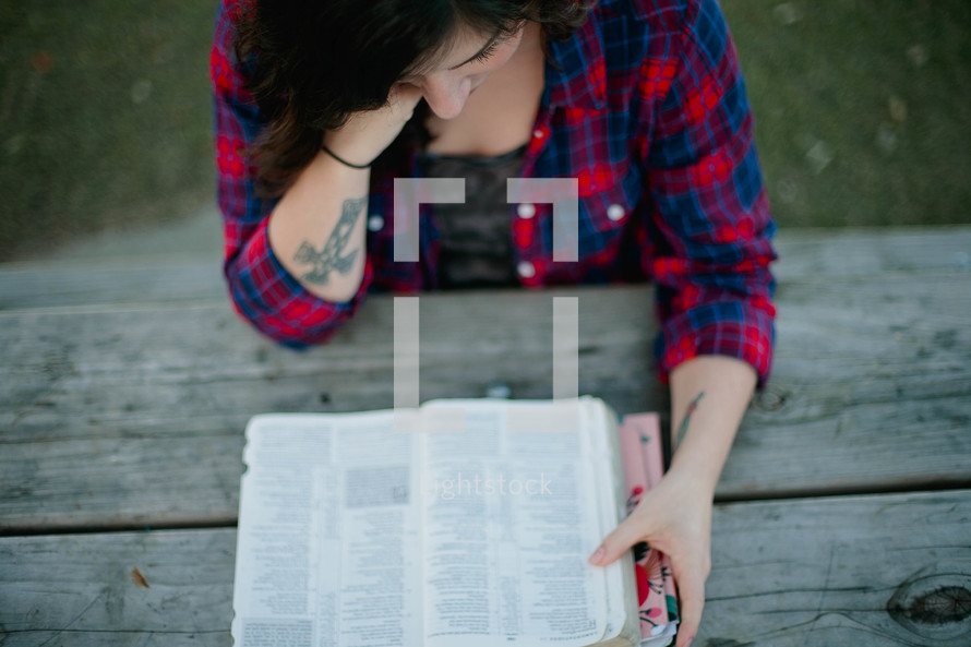 Woman reading the Bible while sitting at a picnic table outside.