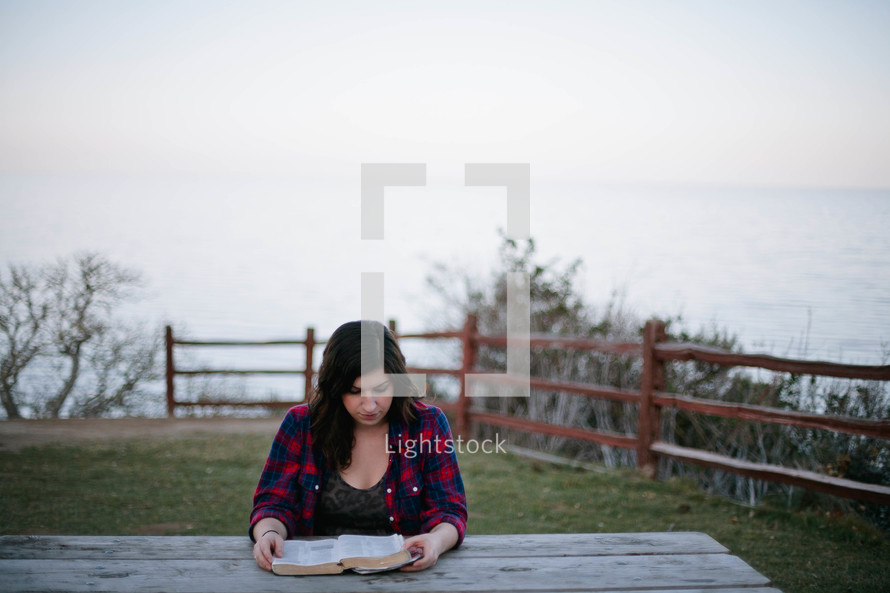 Woman reading the Bible as a picnic table outside.