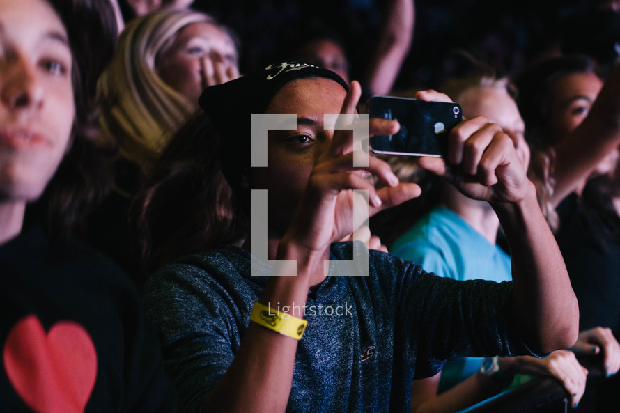 teens in an audience taking pictures with cellphones