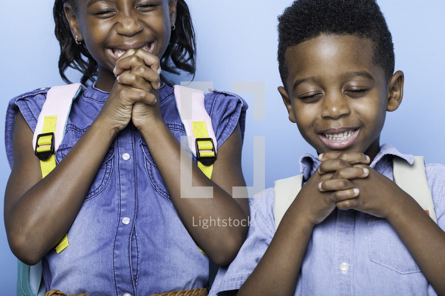 children praying before the first day of school with book bags 