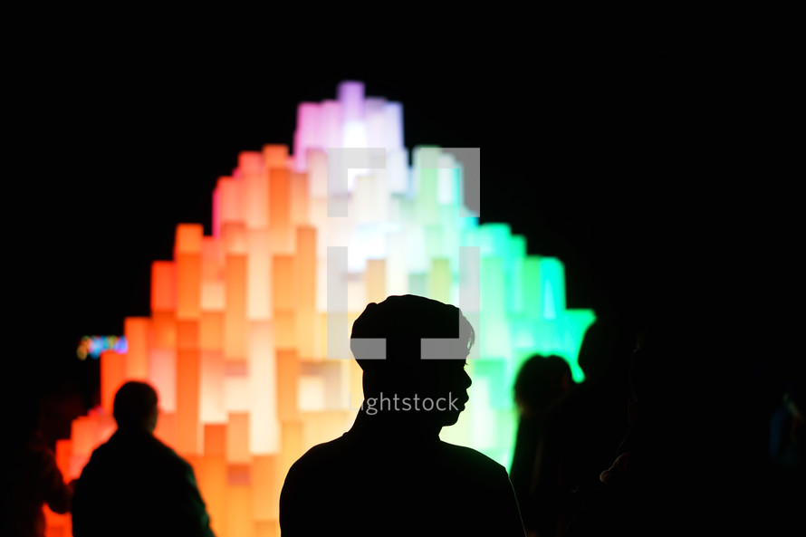 silhouettes in front of a glowing rainbow sculpture 