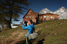 man with a camera standing near a mountain cabin