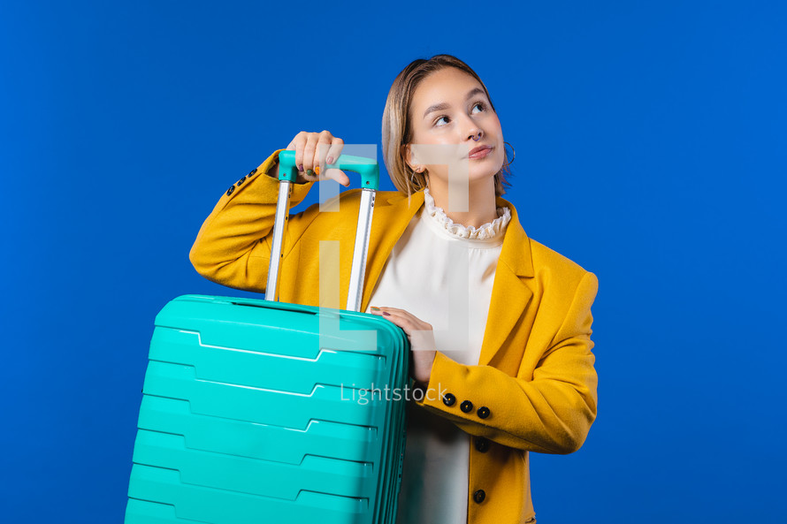 Young pretty woman with carry-on suitcase on blue background. Teenager traveling with blue luggage bag for airplane hand baggage. Summer travel, vacation concept. High quality photo