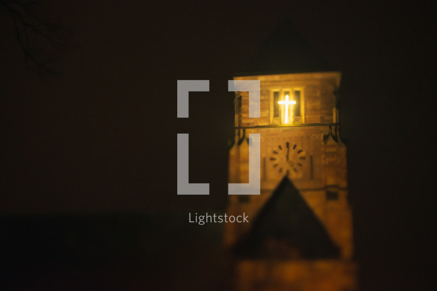 glowing cross on a church bell tower at night 