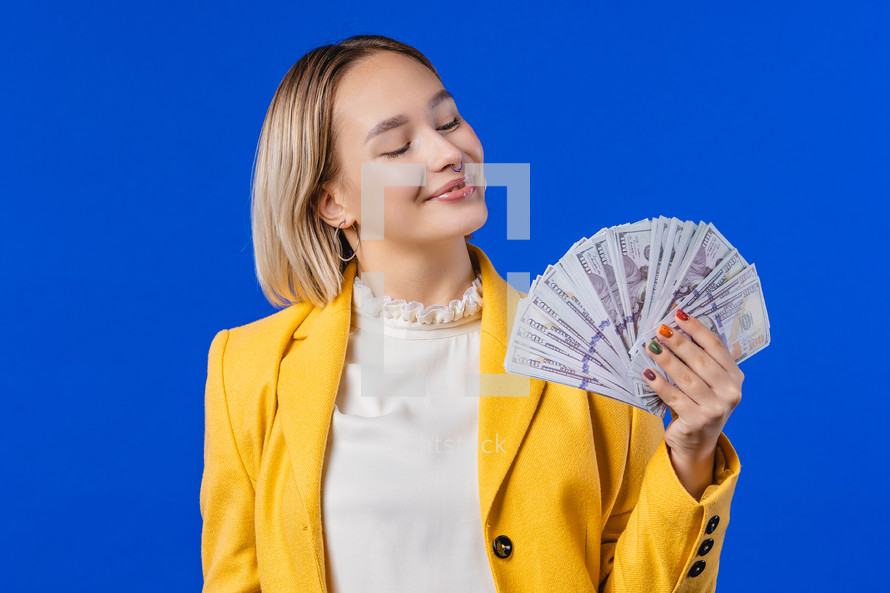 Rich excited blonde woman with cash money - USD currency dollars banknotes on blue wall. Symbol of jackpot, gain, victory, winning lottery. High quality